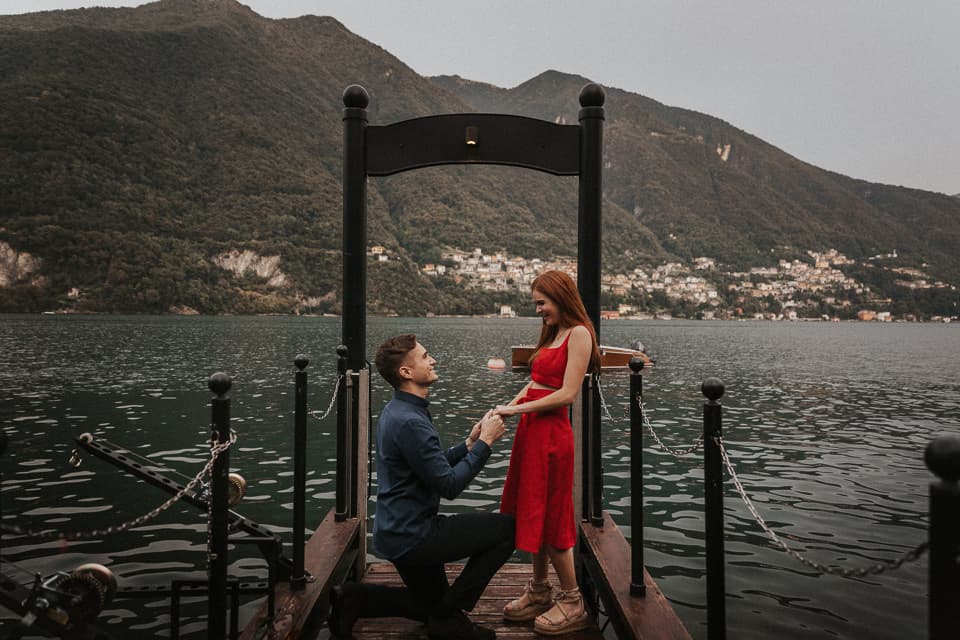 A marriage proposal on a wooden dock over Lake Como, with the mountains and the far shore behind the couple