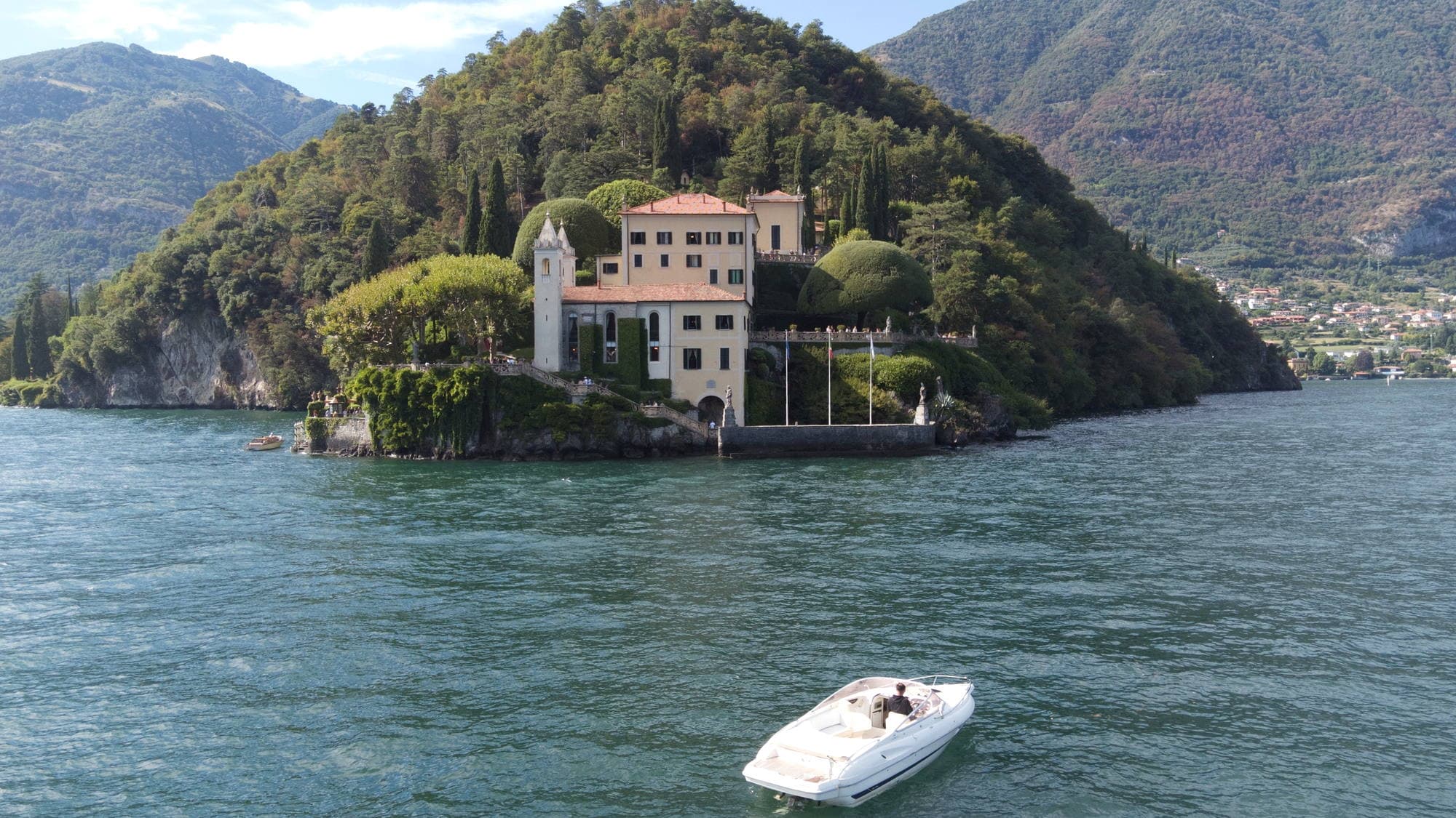 Villa del Balbianello on its wooded peninsula seen from the water, the boat holding offshore on turquoise water